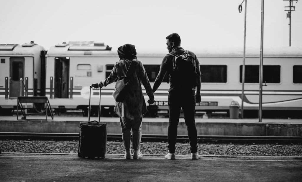 back view of couple holding hands looking on to a train at a terminus